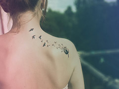 Спина девушки с татуировкой облетающего одуванчика